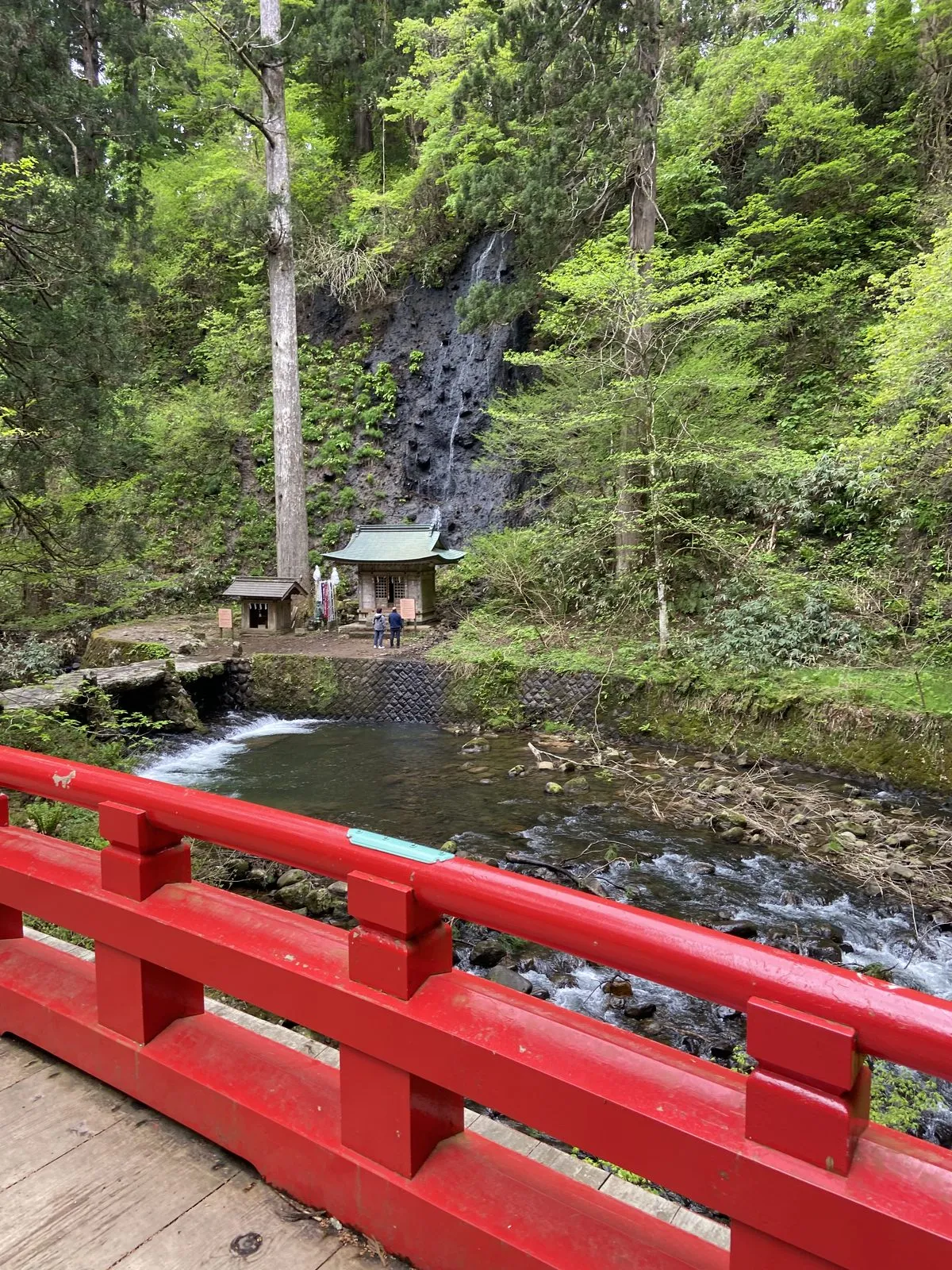Suga Falls seen from the red bridge, a thin waterfall with a small shrine at its base